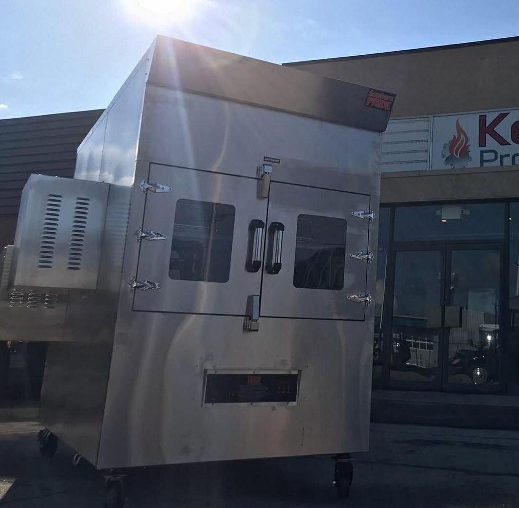 A new Southern Pride SP‑1400 rotisserie smoker sits outside Kendale Products Ltd., reflecting sunlight as it’s positioned for delivery or setup.